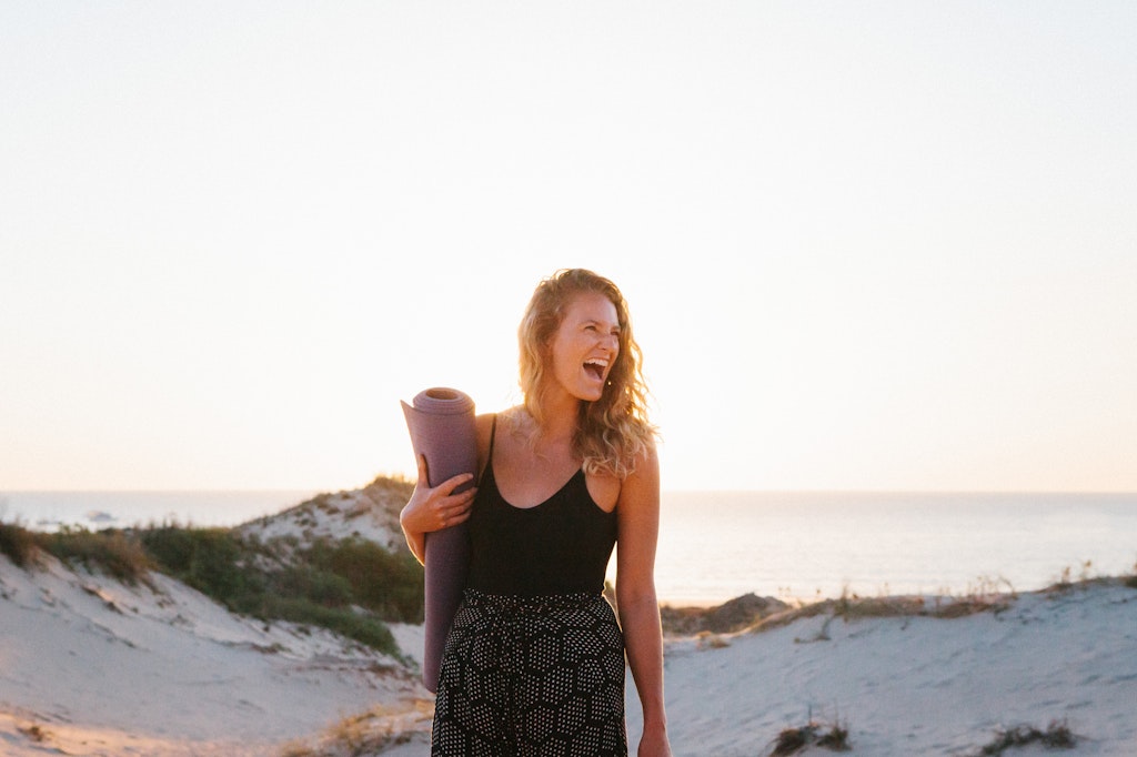 19 - Girl with big smile laughing holding yoga mat overlooking cable beach in Broome, Western Australia.