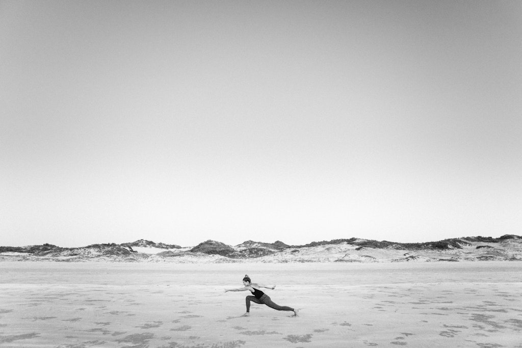 48 - Black and white image of girl doing stretching yoga pose on beach.