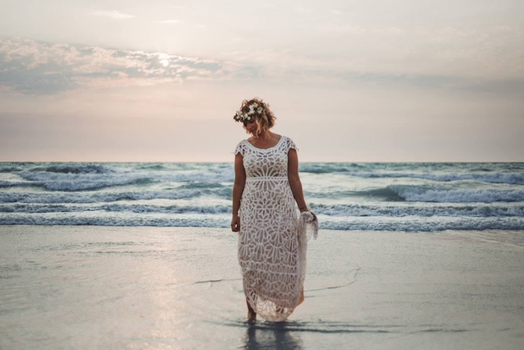 50 - Bride in white custom made wedding dress standing in the water holding the end of her dress wearing a flower crown. Cable Beach, Broome, Western Australia.