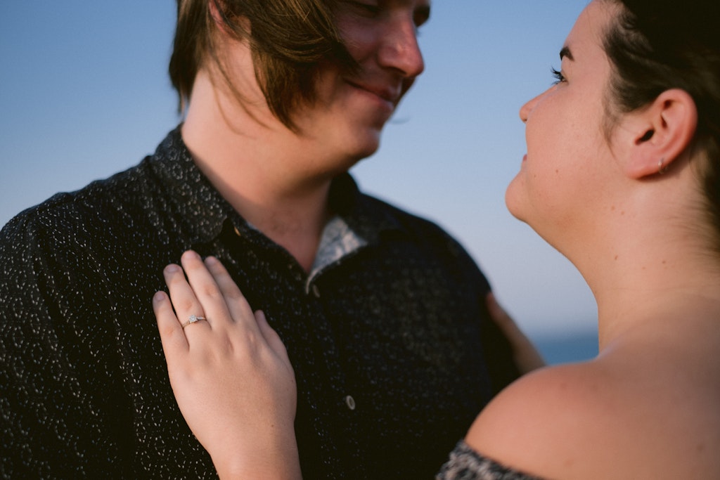 02 - Young engaged couple holding each other with engagement ring being shown off.